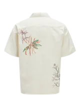 Camisa de manga corta color crema con estampado de flores y hojas en tonos naranja y verde. Tiene cuello resort, cierre frontal con botones y calce relajado.