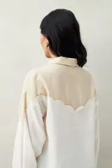 Camisa de lino color crudo y beige, con diseño bicolor y recorte ondulado en el canesú. De silueta relajada, cuenta con mangas amplias y puños camiseros. Se completa con botones de nácar.