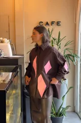 Camisa marrón con rombos rosas en el frente y en los codos, de corte recto y mangas largas.