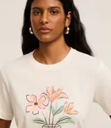 Remera de malla color crudo con estampa de un jarrón con flores, cuello redondo y mangas cortas.