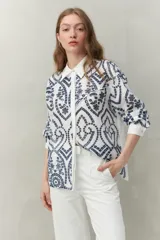 Camisa blanca de manga larga con bordado azul, cuello clásico, recortes que enmarcan la silueta y botones al frente.