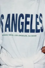Camiseta gris jaspeado de corte amplio, cuello redondo y mangas cortas. Estampado frontal con la frase "Los Angeles 8500 Beverly Blvd, Los Angeles, CA 90048" en color azul.