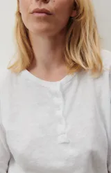 Remera blanca de manga larga con cuello henley y tapeta con botones.