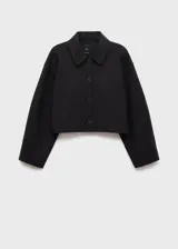 Chaqueta corta de color negro, con cuello camisero, cierre frontal de botones y bolsillos de parche.