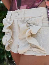Shorts color crema de lino bordado con diseño floral, cintura alta con botón y volados frontales.