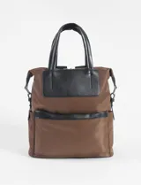 Mochila marrón de tela con detalles en cuero vegano negro, con doble asa de mano y correa de hombro ajustable.
