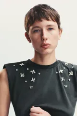 Camiseta negra con efecto lavado, cuello redondo, sisas amplias con hombreras y apliques de joyas combinadas a contraste en la parte superior.