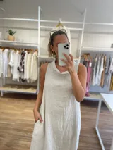 Vestido largo sin mangas color azul claro, confeccionado en lino, con cuello tipo buche o drapeado. Presenta un calce holgado y bolsillos laterales.