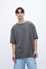 Remera gris de algodón con cuello redondo y calce oversize. Presenta un pequeño parche con diseño en el pecho.