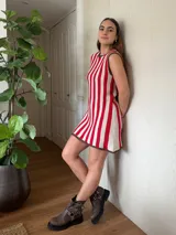 Vestido corto de algodón tejido en punto jersey con diseño de rayas verticales rojas y blancas. Terminaciones en crochet hechas a mano con detalle de lurex. Cuello redondo, sin mangas y silueta trapecio.