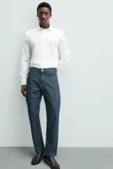 Camisa celeste a rayas verticales blancas, de corte recto, con cuello italiano abierto, mangas largas con puños abotonados y cierre frontal con botones.