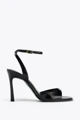 Sandalias negras de charol con efecto craquelado, de tacón fino y punta cuadrada. Cierre con hebilla metálica en la pulsera del tobillo.