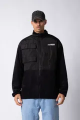 Campera negra con la parte superior de tela tipo rompevientos con dos bolsillos con solapa y la parte inferior de micro polar. Tiene cierre frontal y cuello alto.