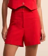 Bermuda roja de sastrería en crepé, con trabillas en la cintura, cierre delantero y bolsillos simulados.