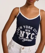 Body de tirantes finos color azul marino con ribete blanco en escote y tirantes. Presenta un estampado grande en blanco con el texto "NEW YORK CITY 1978 NYC Original".