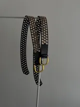 Cinturón negro de cuero ecológico con hebilla metálica dorada y ojales metálicos dorados.