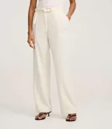 Pantalón de vestir color crudo, de corte recto, con bolsillos laterales y traseros. Se ajusta a la cintura con cinturón de cuero marrón con hebilla dorada.