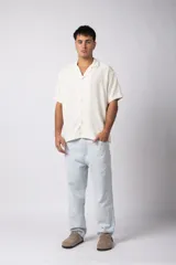 Camisa de manga corta color crudo, confeccionada en lino texturizado. Tiene cuello tipo cubano, cierre frontal con botones y corte recto.