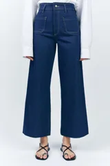 Pantalón de jean de tiro alto color negro con pierna ancha, bolsillos delanteros y traseros, y cierre frontal con cremallera y botón metálico.