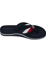 Ojotas de mujer color azul marino con tira de tela trenzada que presenta franjas rojas y blancas, y un dije metálico con el monograma TH en dorado.