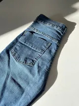 Pantalón de jean de tiro alto, corte flare, color azul oscuro, con costuras frontales y detalle desflecado en el ruedo.