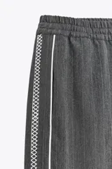 Pantalón de tiro alto negro a rayas verticales blancas, con cintura elástica ajustable con cordones, bolsillos delanteros y banda lateral blanca.