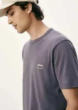Remera gris con cuello redondo y manga corta. Presenta un pequeño parche con logo en el pecho.