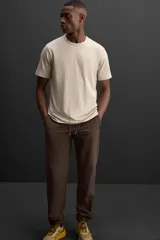 Pantalón deportivo color marrón oscuro, corte regular fit, confeccionado en tejido técnico ligero y elástico. Cuenta con cintura elástica ajustable con cordón, bolsillos frontales con cierre de cremallera, bolsillo trasero con cierre de cremallera oculta en costura y bajo ajustable con elástico.