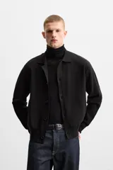 Camisa de punto color negro, corte relaxed fit, con cuello solapa, manga larga y cierre frontal con botones.