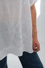 Blusa blanca de lino con cuello redondo, mangas cortas, bolsillo en el pecho y detalle de bordado calado en el lateral inferior. Corte holgado.