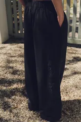 Pantalón negro con bordados florales en los laterales, tiro alto, cintura elástica en la parte trasera, bolsillos laterales, pliegues y cierre frontal con cremallera, botón interior y gancho metálico.