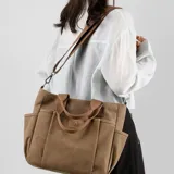 Bolso de lona color marrón con múltiples bolsillos externos frontales y laterales. Posee asas de mano y una correa larga ajustable y extraíble.