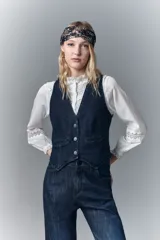 Chaleco sastrero de denim azul oscuro con elastano, acceso con botones con logo, falsos bolsillos ojal y tira de ajuste en la espalda con hebilla. Bordado de alas en la espalda.