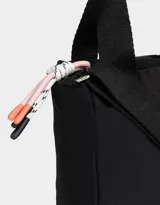 Cartera bandolera negra de tela deportiva con doble asa corta de mano, correa regulable y desmontable, cierre superior y tag de goma con logo.