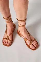 Sandalia de cuero color marrón con tiras finas y cordones para atar al tobillo.