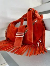 Cartera bandolera color naranja de gamuza con flecos, cierre superior con cremallera y asa de hombro ajustable.