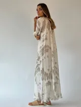 Vestido largo color beige con estampado tie-dye en tonos rosados, corte amplio, mangas cortas con volados y ruedo con flecos.