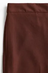 Pantalón ancho color marrón chocolate, de tiro alto con elástico en la parte posterior de la cintura y cierre oculto con corchete en un lado. Presenta bolsillos laterales discretos y piernas amplias con pliegues adelante y atrás.