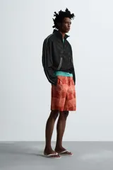Short de baño color ladrillo con estampado de líneas curvas en color salmón. Tiene cintura elástica ajustable con cordón, bolsillos laterales y trasero.