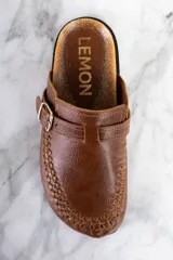 Zueco de cuero color marrón con diseño trenzado en la puntera, hebilla metálica ajustable y plantilla de corcho.