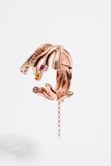 Pulsera ancha con apertura de bisagra, en metal con acabado en oro rosado, decorada con texturas, cadenas y cristales.