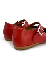 Zapato tipo Mary Jane color rojo, de cuero, con punta redondeada y tira sobre el empeine con hebilla metálica cuadrada.