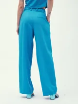 Pantalón de vestir color crema, de corte ancho y tiro alto, con pinzas delanteras y cinturón fino de cuero marrón.
