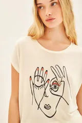 Remera color crema de calce suelto, confeccionada en viscosa. Tiene escote redondo, manga corta y estampa frontal centrada con bordado.