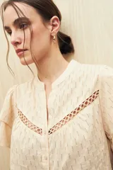 Camisa blanca de algodón liviano con diseño calado, cuello mao, mangas cortas abullonadas y detalle de pasamanería en el frente.