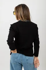 Campera negra con cuerpo de cuero y mangas de tejido de punto. Tiene cuello redondo, cierre frontal con cremallera, dos bolsillos con cremallera en el pecho y costuras decorativas en los hombros.