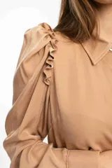 Camisa tipo seda color crema, con volados en el hombro y frunce en la manga, diseño elegante.