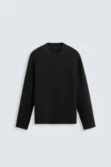 Jersey negro de punto con textura, corte holgado, cuello redondo y mangas largas.