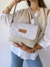 Bandolera color crudo con solapa de gamuza y cuerpo de cuero sintético texturizado. Tiene correa corta de cuero con tientos y forro de tela con bolsillo interno.
