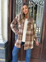 Sobrecamisa marrón con estampado de cuadros blancos, corte recto, cuello camisero, cierre frontal con botones y bolsillos de parche en el pecho.